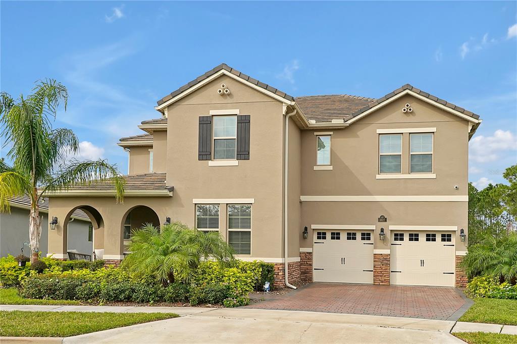 A two-story suburban house with a tan stucco exterior, stone accents, and a two-car garage — 9827 BEACH PORT DRIVE, WINTER GARDEN, FL