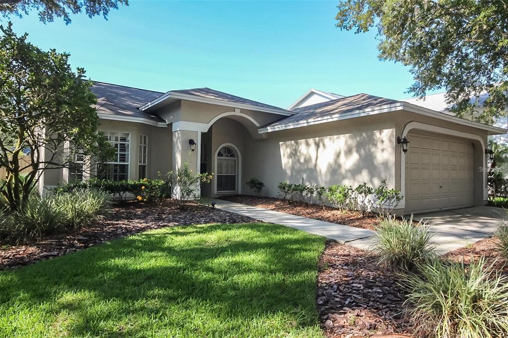 A single-story house with a beige stucco exterior, a two-car garage, and a front walkway — 17765 OAK BRIDGE STREET, TAMPA, FL