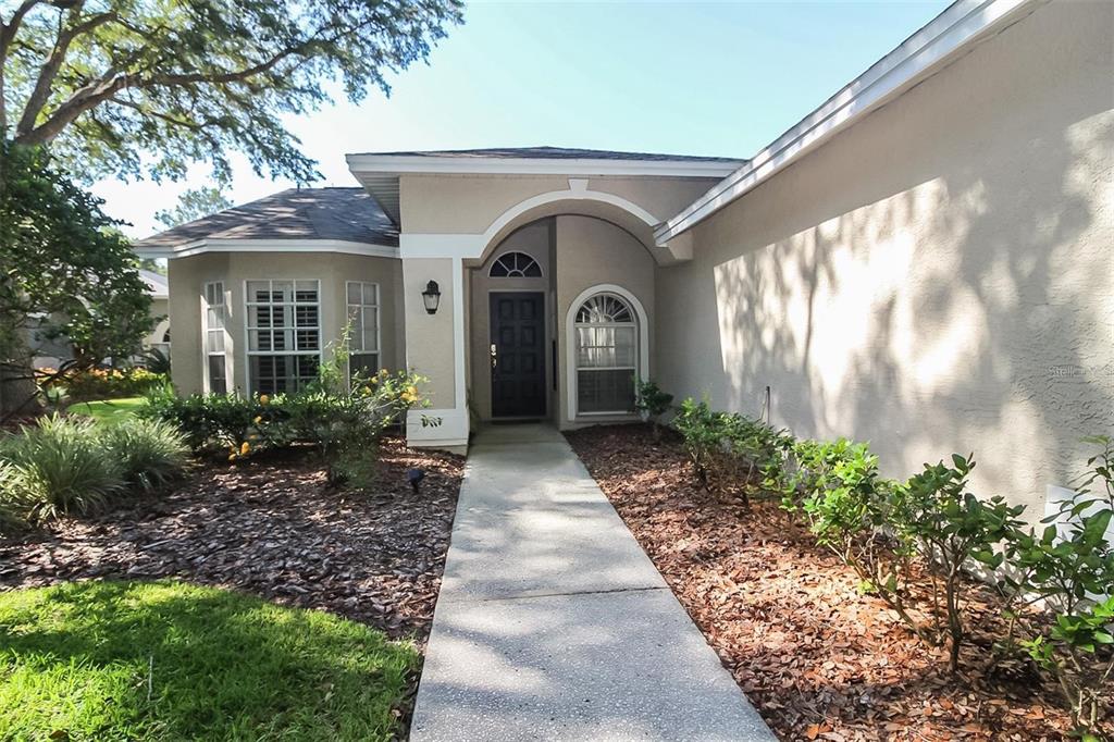 A concrete walkway leads to the front entrance of a beige house with arched details — 17765 OAK BRIDGE STREET, TAMPA, FL