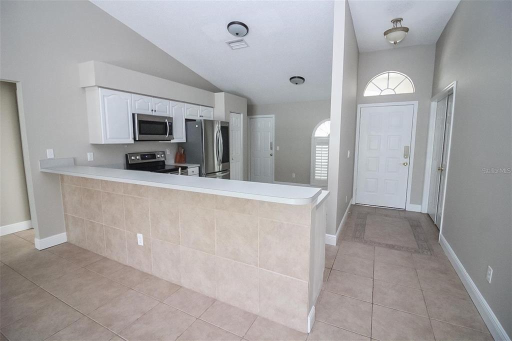A kitchen with a tiled breakfast bar, white cabinets, and stainless steel appliances near an entryway — 17765 OAK BRIDGE STREET, TAMPA, FL