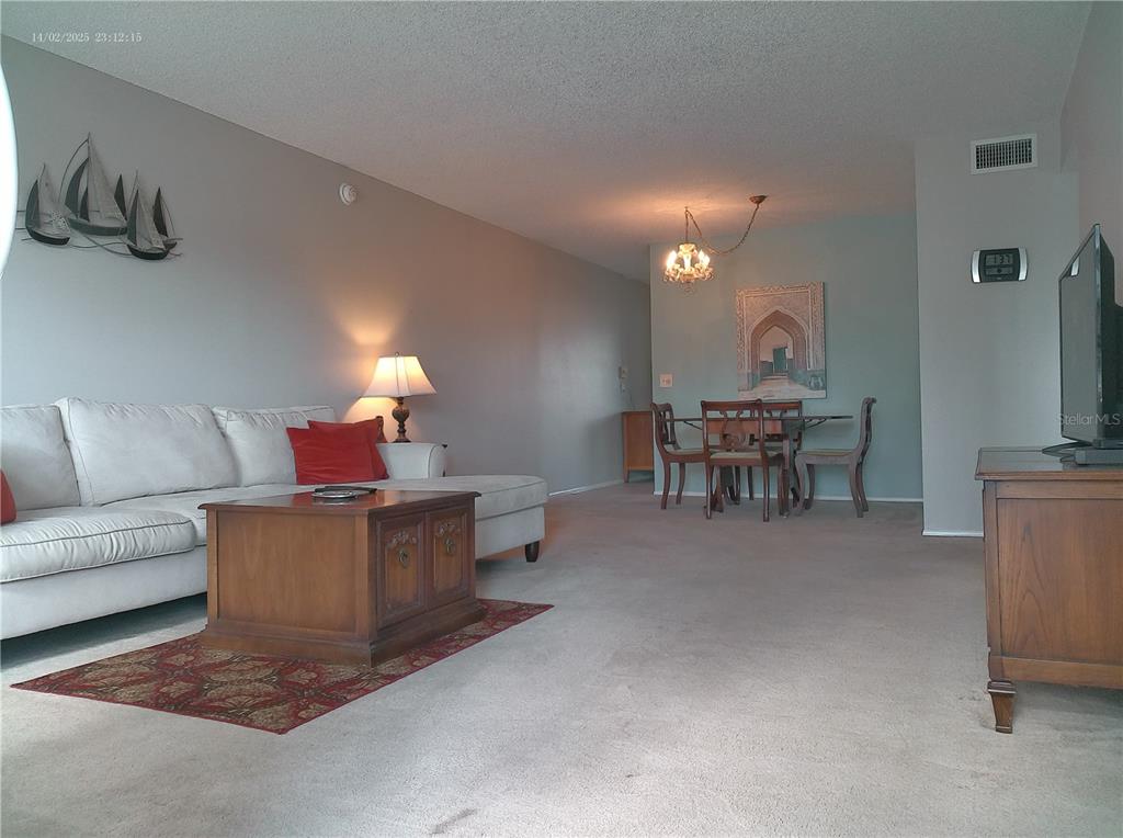 A living room with a white sectional sofa, wooden coffee table, and a dining area — 2456 ECUADORIAN WAY UNIT 38, CLEARWATER, FL