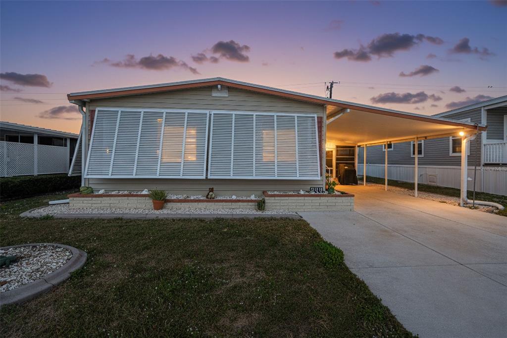 A single-story mobile home with a carport, beige siding, and white shutters at dusk — 320 LA COSTA, NORTH PORT, FL