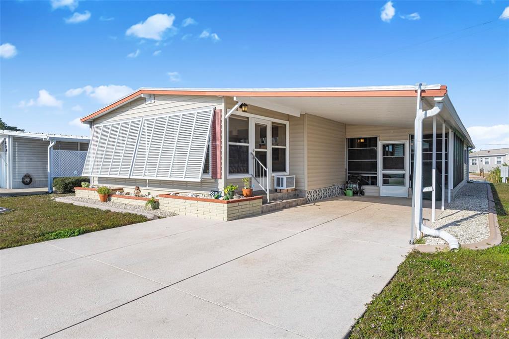 A single-story manufactured home with a concrete driveway, carport, and a brick-bordered front garden — 320 LA COSTA, NORTH PORT, FL