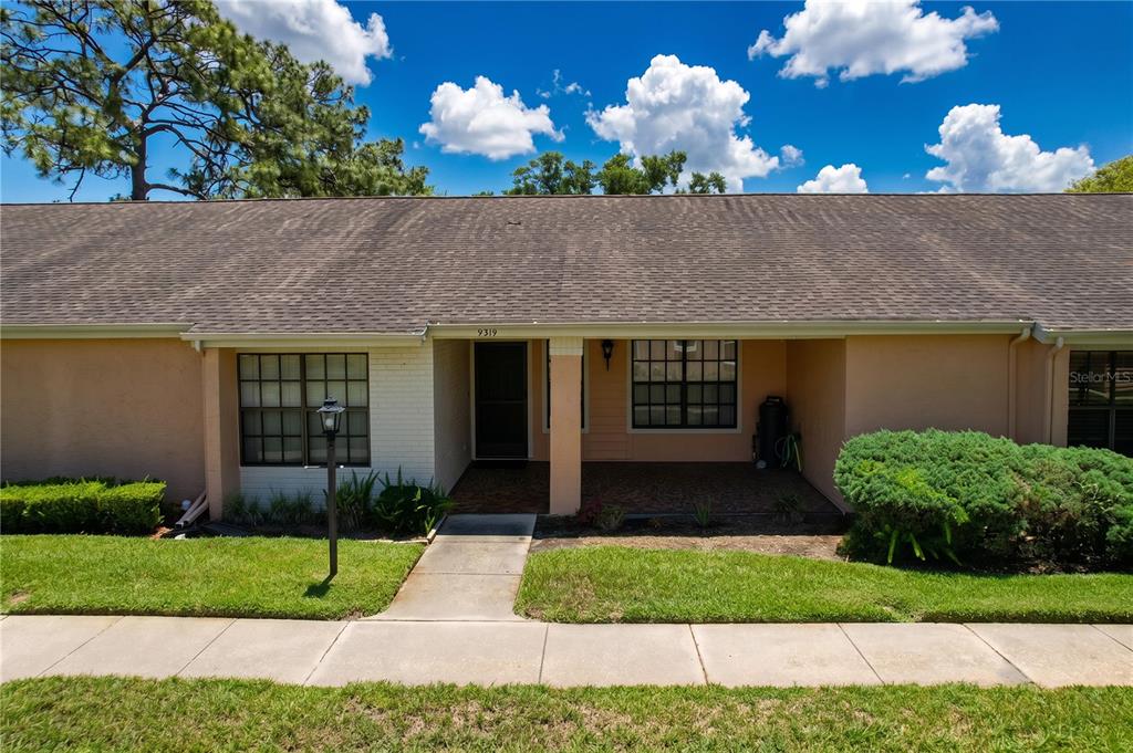 The exterior of a single-story house features a covered entryway, brick patio, and lawn — 9319 TROWBRIDGE COURT, NEW PORT RICHEY, FL