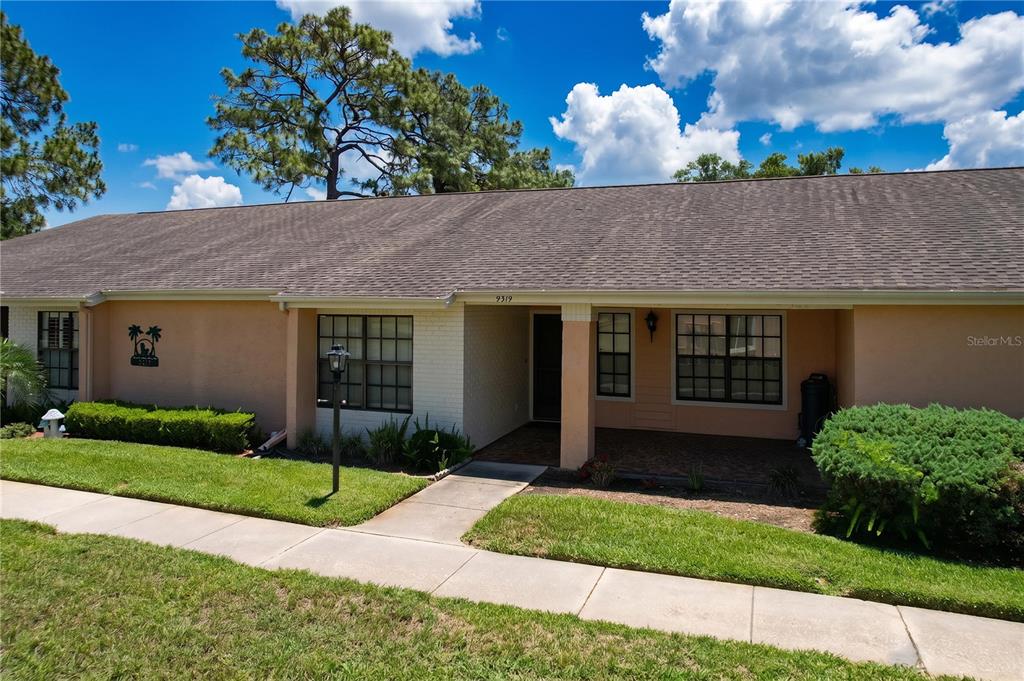 A single-story house with a tan stucco exterior, a shingled roof, and a front porch — 9319 TROWBRIDGE COURT, NEW PORT RICHEY, FL