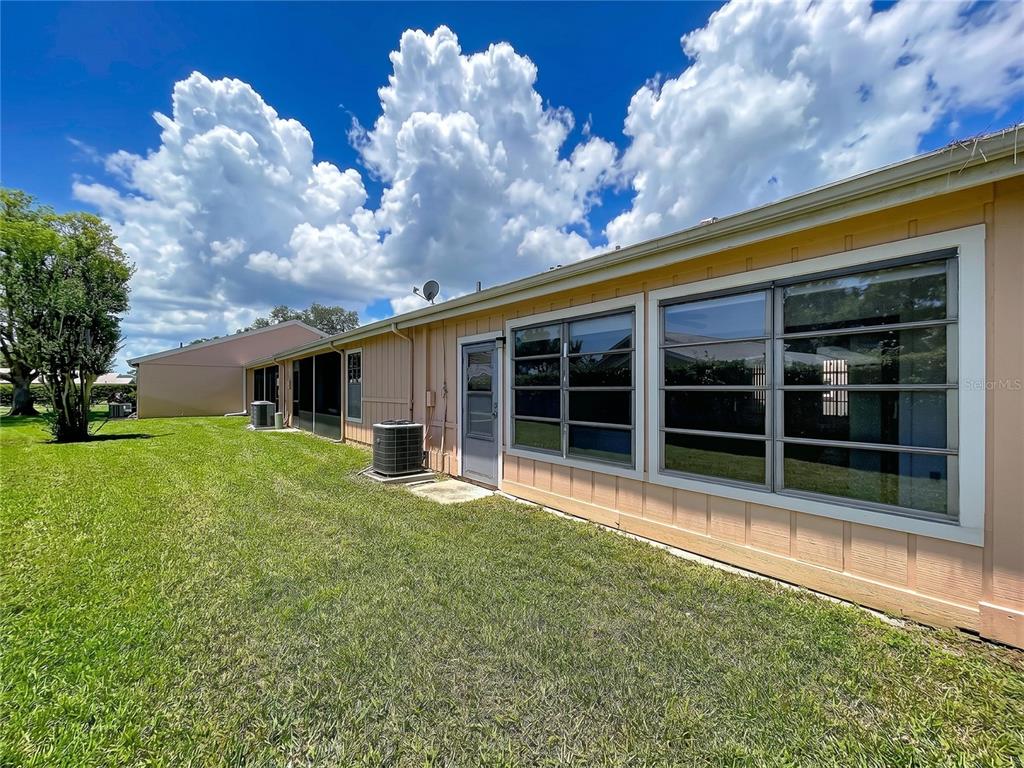 The exterior of a house features tan siding, large windows, a screen door, and air conditioning units — 9319 TROWBRIDGE COURT, NEW PORT RICHEY, FL