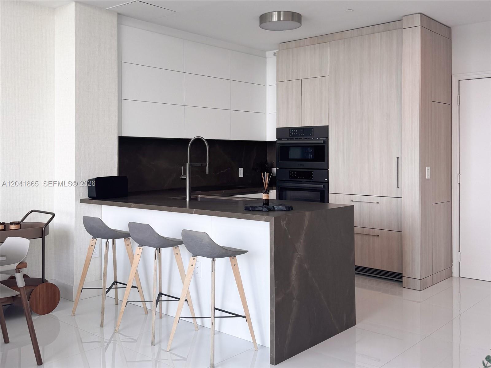 A modern kitchen features a dark stone island, white upper cabinets, and light wood cabinetry — 950 Brickell Bay Dr # 5608, Miami FL 33131, MIAMI, FL
