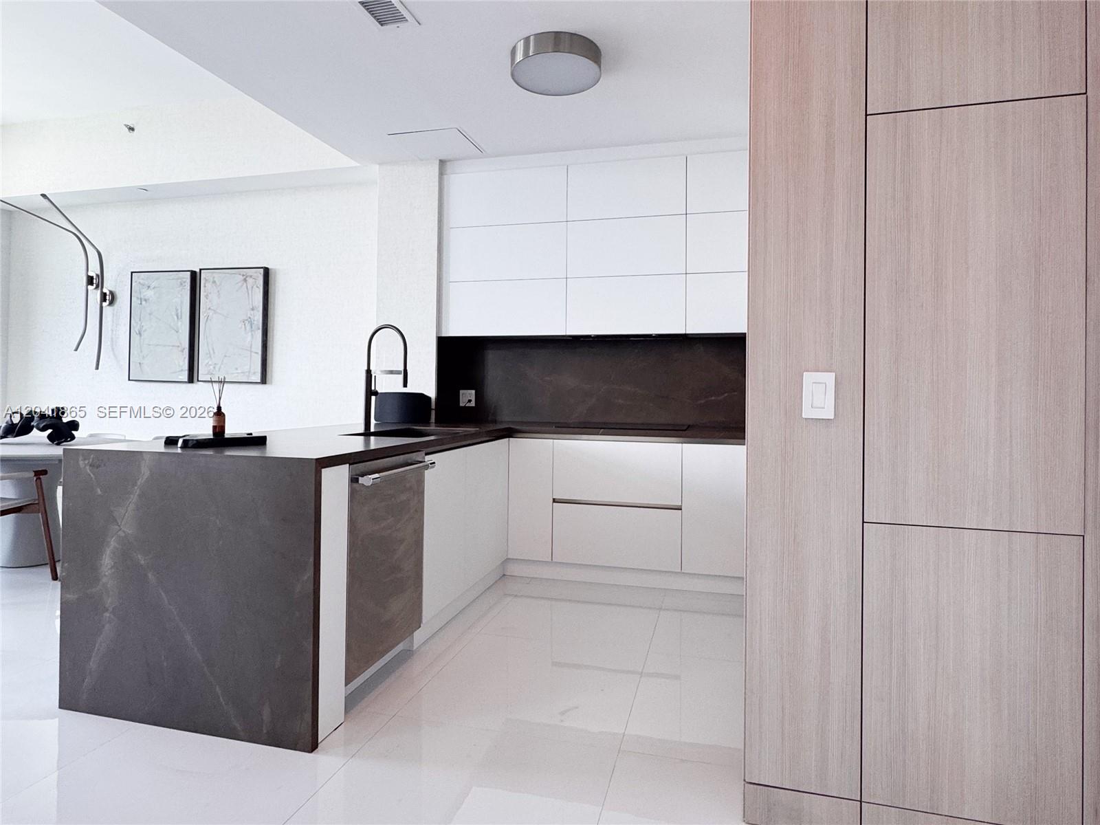 A modern kitchen features white cabinets, a dark stone island, and light wood paneling — 950 Brickell Bay Dr # 5608, Miami FL 33131, MIAMI, FL