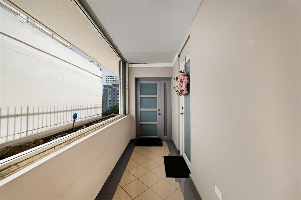 A narrow balcony with tiled flooring, a gray door, and a view of nearby buildings — 1422 WILSON AVENUE AVENUE UNIT 5B, SAN JUAN, PR