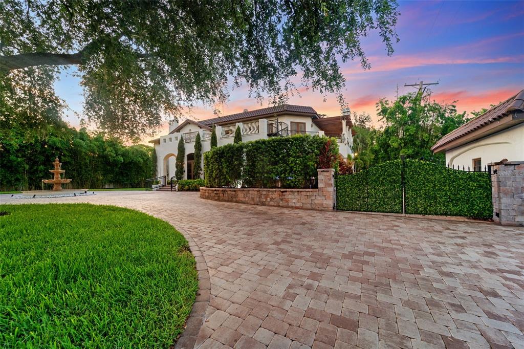 A paved driveway leads to a two-story Mediterranean-style house with a fountain and lush landscaping — 4555 W SWANN AVENUE, TAMPA, FL