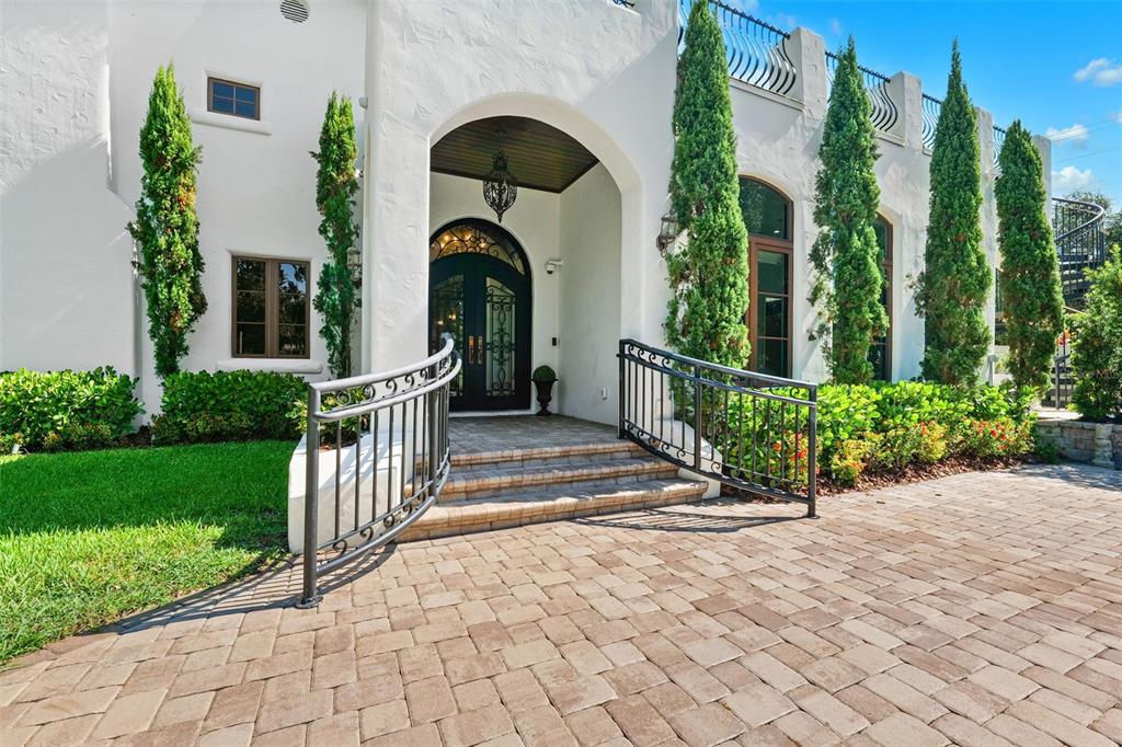 The exterior of a white stucco house features an arched entryway, stone steps, and landscaping — 4555 W SWANN AVENUE, TAMPA, FL