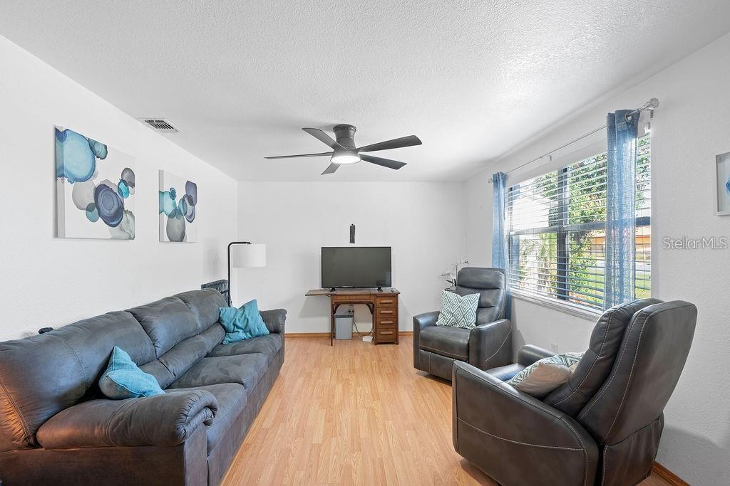 A living room features a dark gray sofa, two matching recliners, and wood-look flooring — 1105 58TH STREET S, ST PETERSBURG, FL