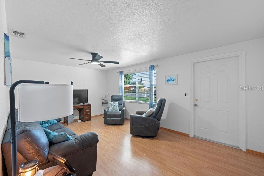 A living room with light wood flooring, a ceiling fan, two recliners, and a sofa — 1105 58TH STREET S, ST PETERSBURG, FL