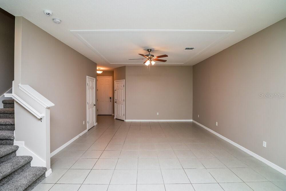 An empty living room features beige walls, light tile flooring, and a ceiling fan — 1310 E 10TH STREET, APOPKA, FL