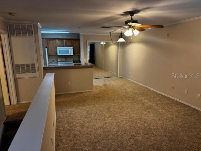 A carpeted living room with a ceiling fan opens to a kitchen with wooden cabinets — 4850 51ST STREET W UNIT 4207, BRADENTON, FL