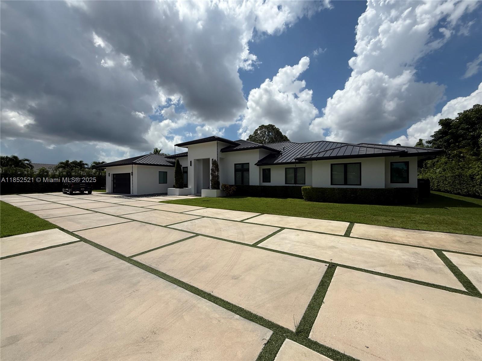 A modern single-story house with a large concrete paver driveway and a dark metal roof — 9600 SW 66th St, Miami FL 33173, MIAMI, FL