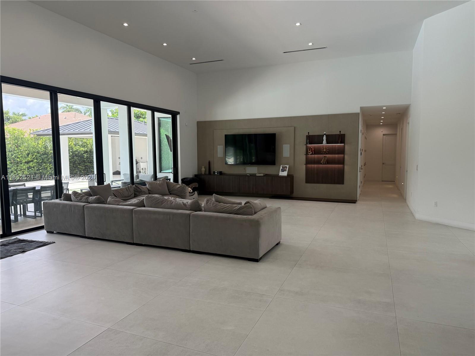 A spacious living room features a large sectional sofa, a wall-mounted television, and floor-to-ceiling glass doors — 9600 SW 66th St, Miami FL 33173, MIAMI, FL