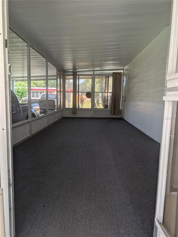 A screened-in porch features gray carpeting, white walls, and a view of parked vehicles — 469 NE 64TH AVENUE, OCALA, FL