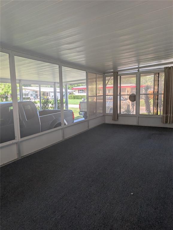 A screened-in porch features gray carpeting, white framing, and a view of parked vehicles outside — 469 NE 64TH AVENUE, OCALA, FL