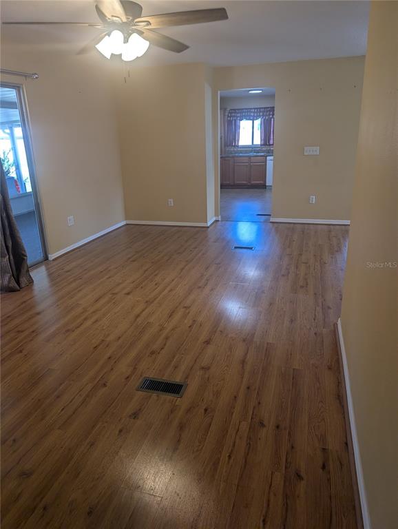 A living room with wood-look flooring, a ceiling fan, and a view into the kitchen — 469 NE 64TH AVENUE, OCALA, FL