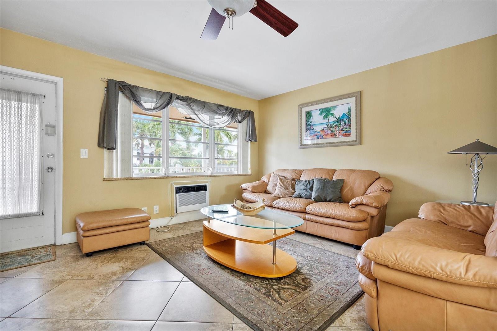 A living room with tan walls, tile floors, leather sofas, and a window air conditioner — 500 Layne Boulevard # 18, Hallandale Beach FL 33009, HALLANDALE BEACH, FL