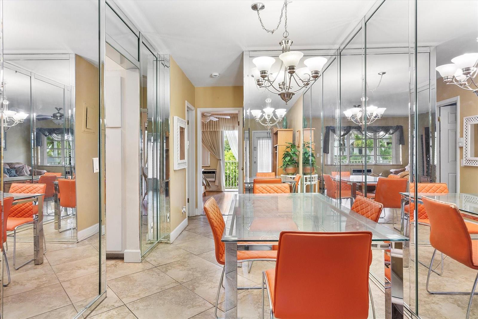 A dining room features a glass table, orange chairs, tiled floors, and mirrored wall panels — 500 Layne Boulevard # 18, Hallandale Beach FL 33009, HALLANDALE BEACH, FL