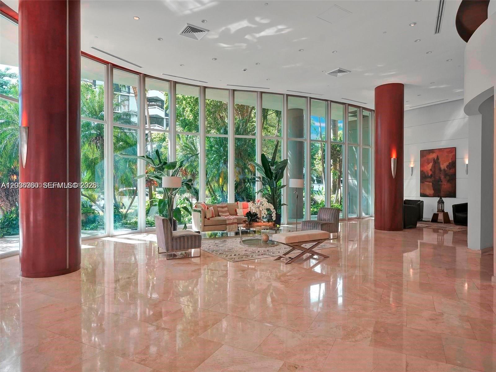 A spacious lobby features floor-to-ceiling windows, polished marble floors, and large red columns — 2475 Brickell Ave # 804, Miami FL 33129, MIAMI, FL