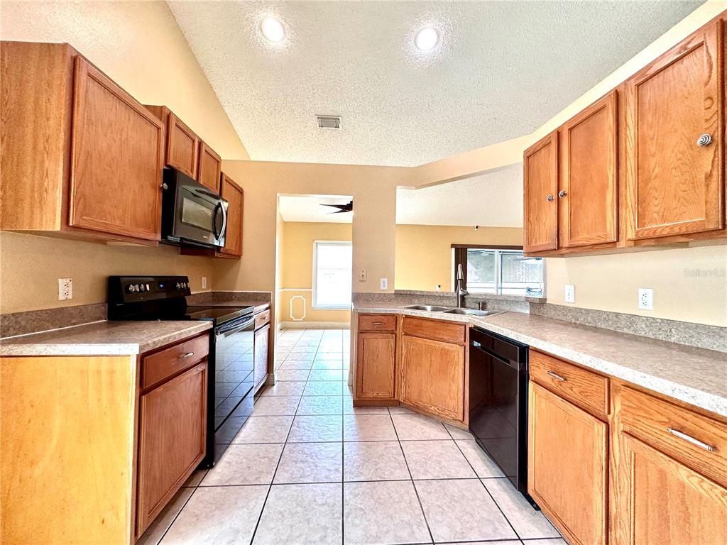 A kitchen features light wood cabinets, laminate countertops, black appliances, and tiled flooring — 1650 NAVIGATOR LANE, TARPON SPRINGS, FL