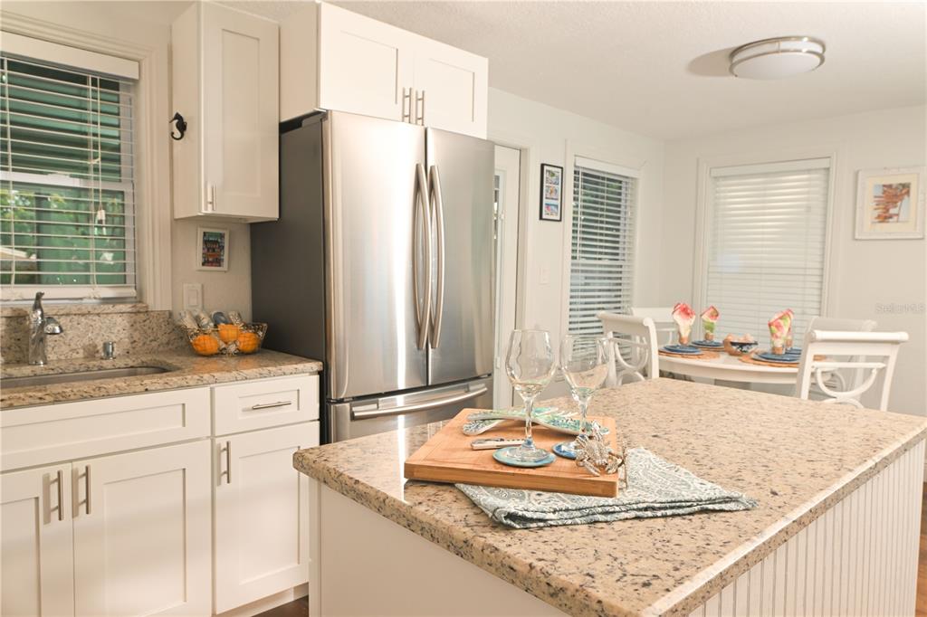 A kitchen features white cabinets, granite countertops, a stainless steel refrigerator, and a center island — 621 MEHLENBACHER ROAD, BELLEAIR BLUFFS, FL