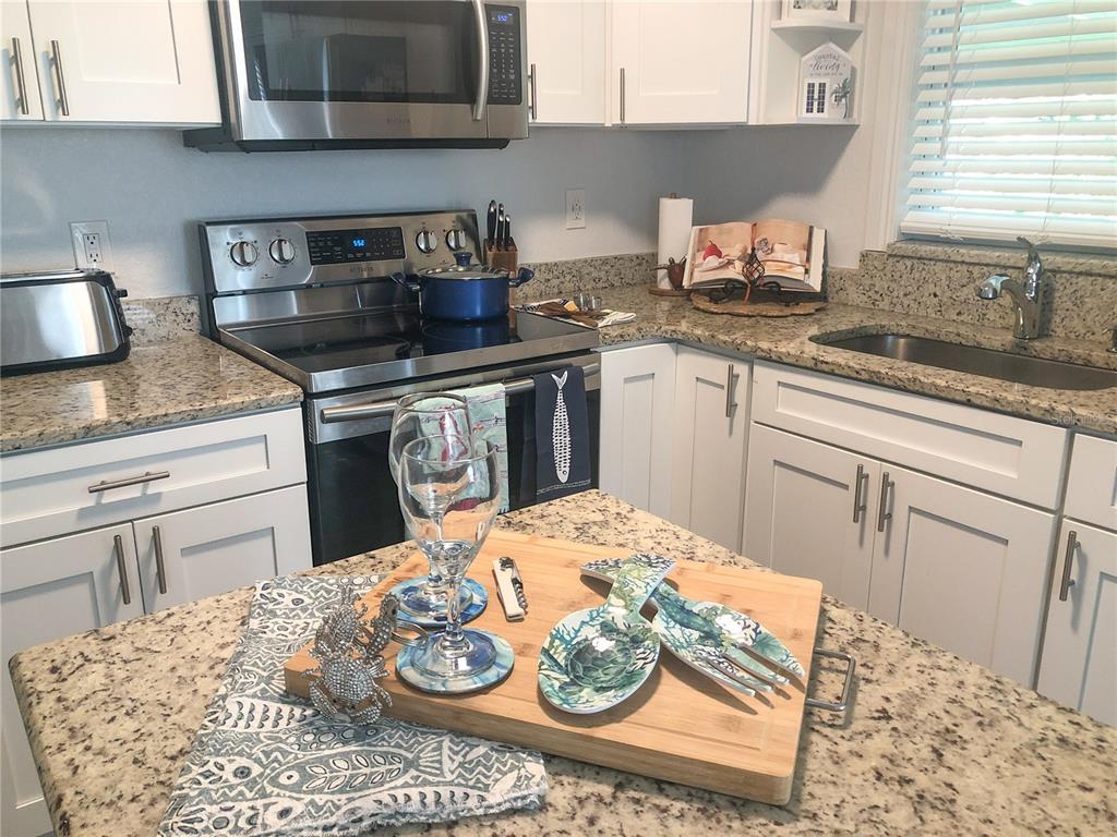 A kitchen with white cabinets, granite countertops, stainless steel appliances, and a window above the sink — 621 MEHLENBACHER ROAD, BELLEAIR BLUFFS, FL