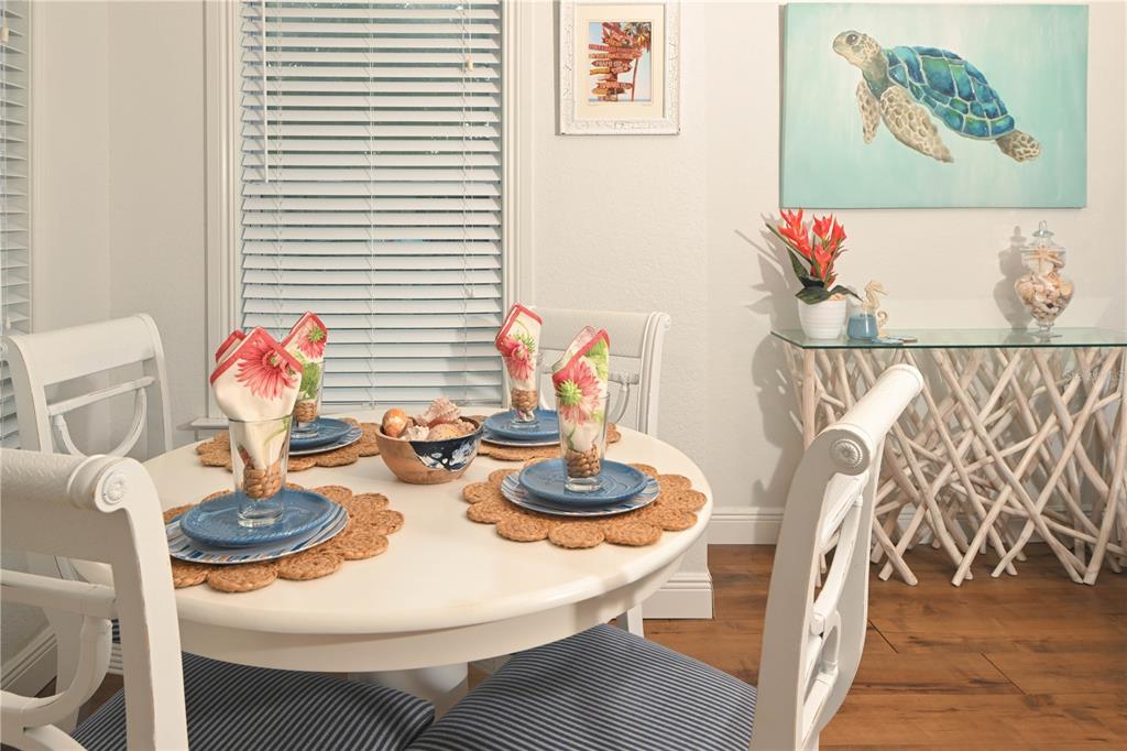 A dining area features a white round table, four chairs, and two windows with outdoor views — 621 MEHLENBACHER ROAD, BELLEAIR BLUFFS, FL