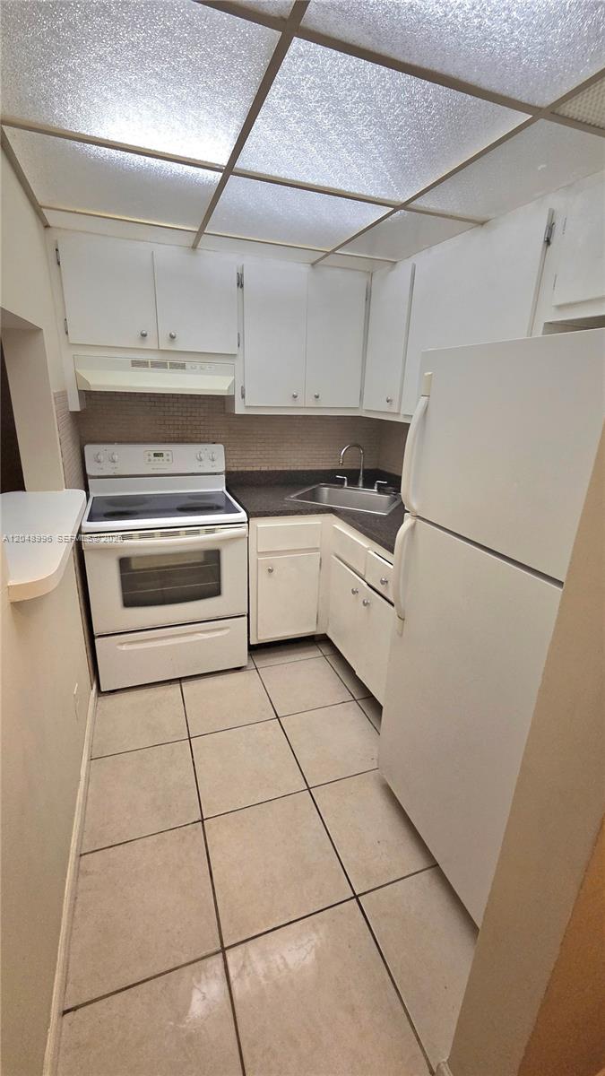 A small kitchen features white cabinets, a white stove, a refrigerator, and a corner sink — 201 SE 6th Ave # 11, Pompano Beach FL 33060, POMPANO BEACH, FL