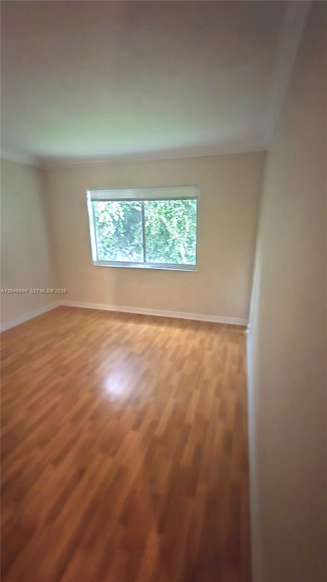 An empty bedroom features light-colored walls, crown molding, and wood-look laminate flooring — 201 SE 6th Ave # 11, Pompano Beach FL 33060, POMPANO BEACH, FL
