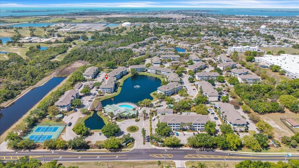 Aerial view of a multi-building apartment complex surrounding a central lake with a pool — 4802 51ST STREET W UNIT 1916, BRADENTON, FL