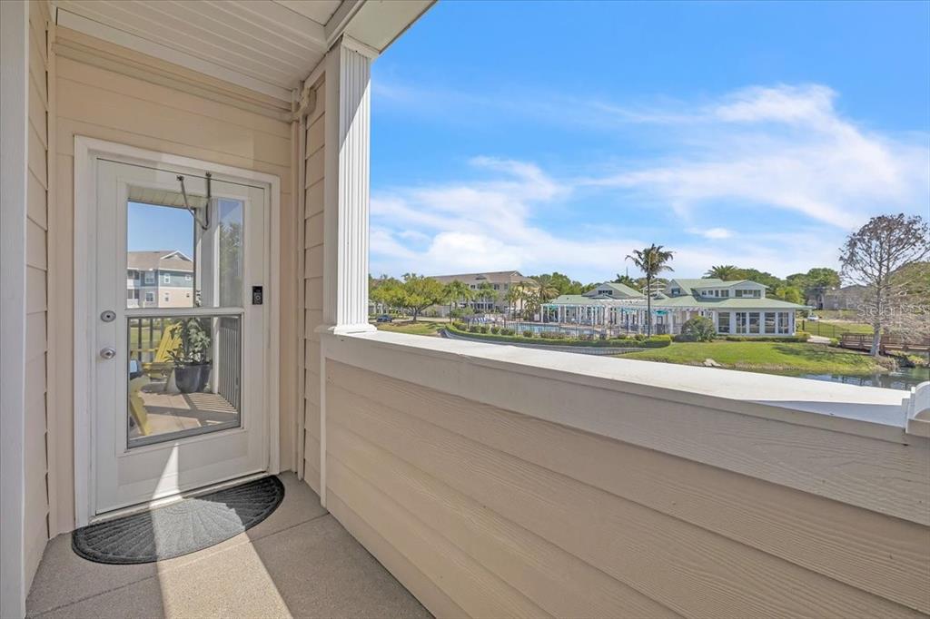 A balcony with a door overlooks a pond and a community clubhouse under a blue sky — 4802 51ST STREET W UNIT 1916, BRADENTON, FL