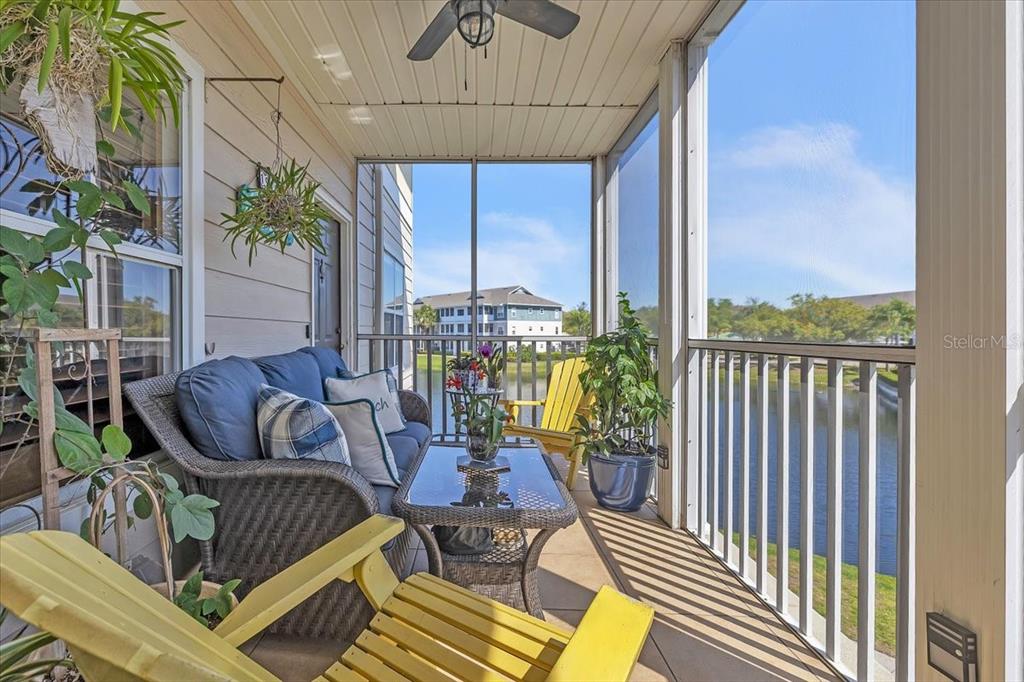 A screened-in balcony features wicker furniture, yellow chairs, and a view of a pond — 4802 51ST STREET W UNIT 1916, BRADENTON, FL