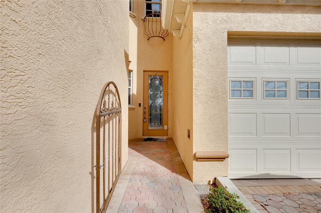 A paved walkway leads to a front door nestled between a stucco wall and a garage — 3975 SQUARE EAST LANE UNIT 9, SARASOTA, FL