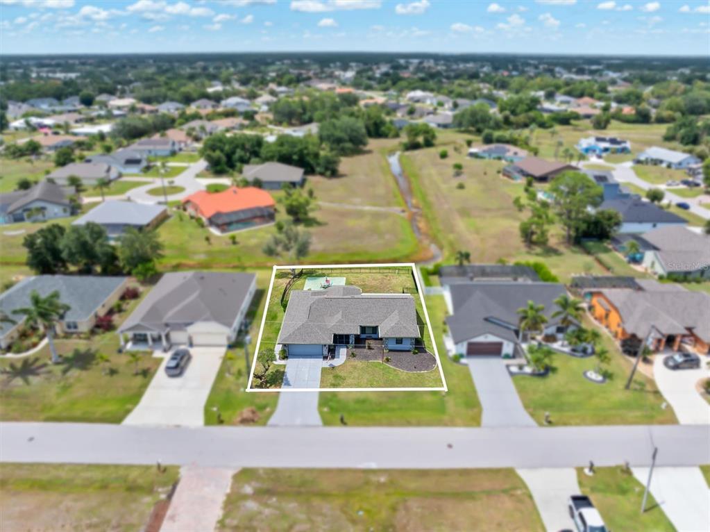 An aerial view shows a single-story house with a gray roof and a fenced backyard — 25106 BOLIVAR DRIVE, PUNTA GORDA, FL