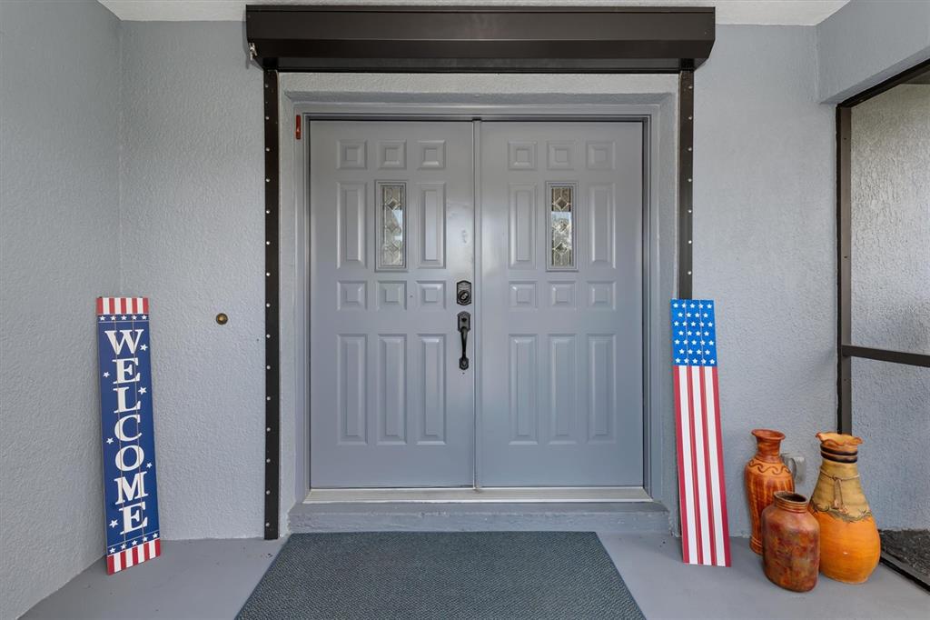 A gray double front door features decorative glass panels and patriotic welcome signs on the porch — 25106 BOLIVAR DRIVE, PUNTA GORDA, FL