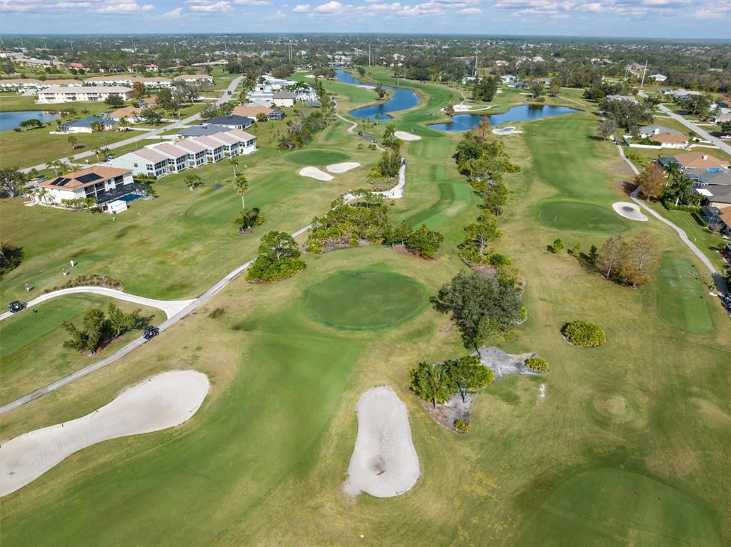 An aerial view of a golf course fairway with sand traps, trees, and surrounding residential buildings — 25106 BOLIVAR DRIVE, PUNTA GORDA, FL