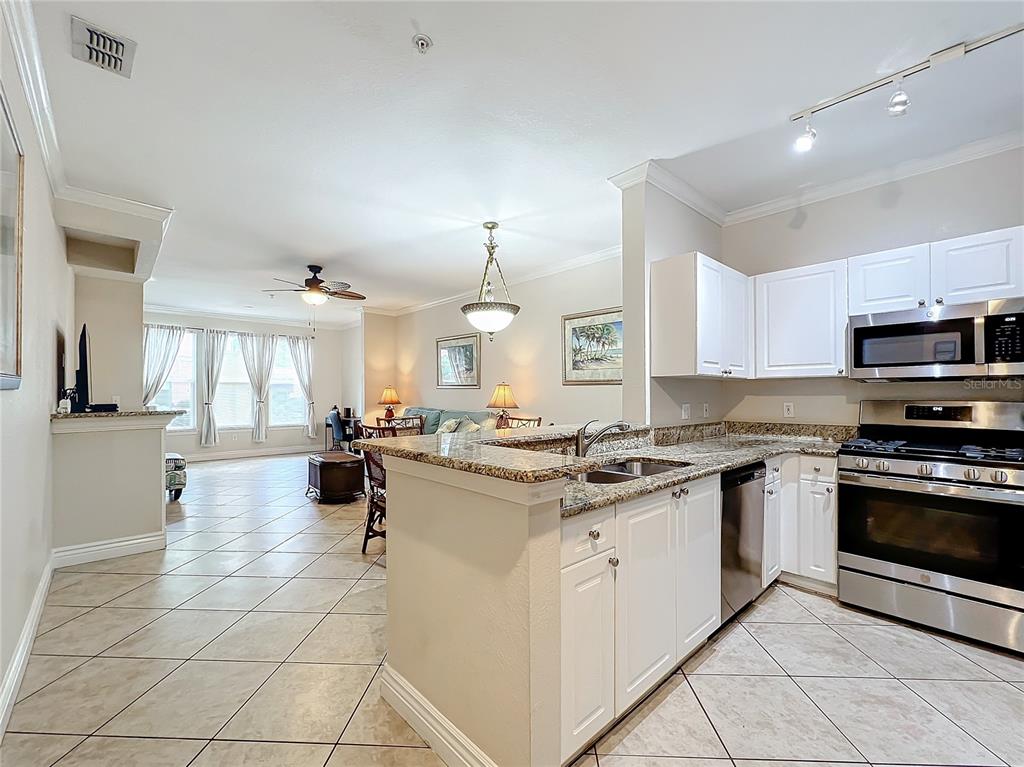 A kitchen with white cabinets and granite countertops opens into a living and dining area — 2724 VIA MURANO UNIT 615, CLEARWATER, FL