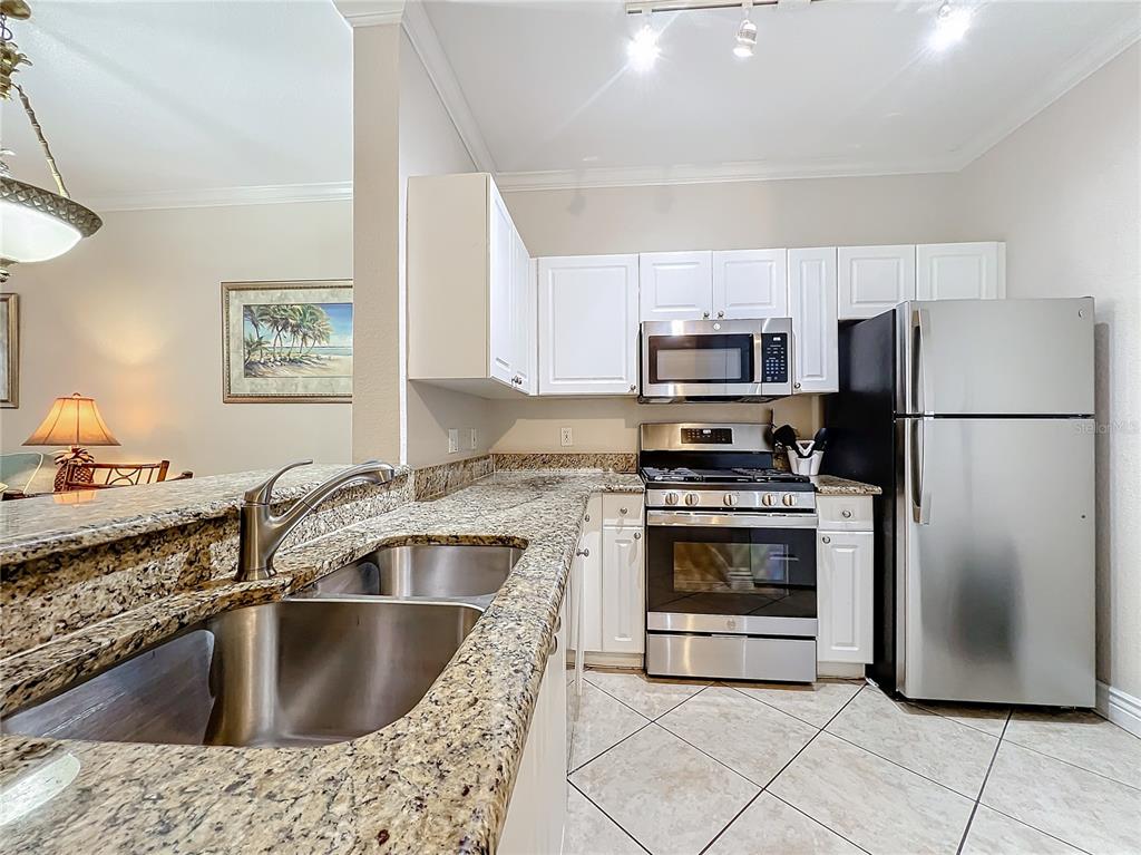 A kitchen features granite countertops, white cabinets, stainless steel appliances, and tile flooring — 2724 VIA MURANO UNIT 615, CLEARWATER, FL