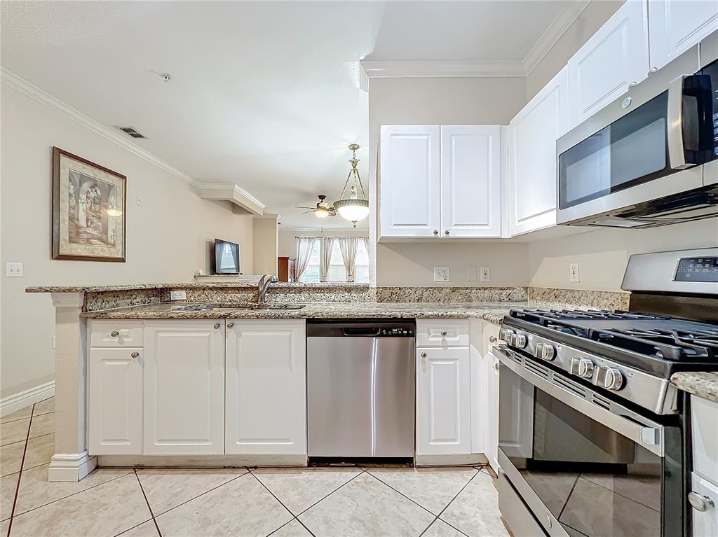 A kitchen features white cabinets, granite countertops, stainless steel appliances, and tile flooring — 2724 VIA MURANO UNIT 615, CLEARWATER, FL