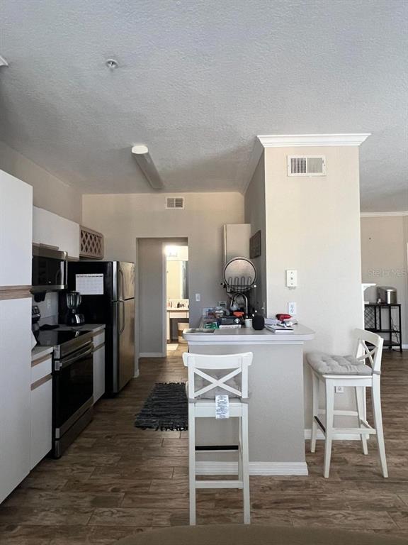 A kitchen features white cabinets, stainless steel appliances, a breakfast bar, and wood-look flooring — 2632 ROBERT TRENT JONES DRIVE UNIT 134, ORLANDO, FL