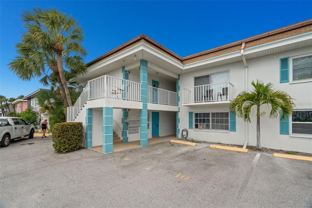 A two-story apartment building with white stucco walls, blue shutters, and an exterior staircase — 11655 3RD STREET E UNIT 1, TREASURE ISLAND, FL