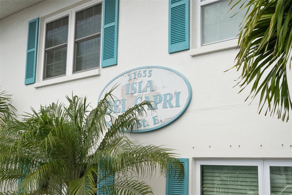 An oval sign reading Isla Del Capri is mounted on the white stucco exterior wall — 11655 3RD STREET E UNIT 1, TREASURE ISLAND, FL