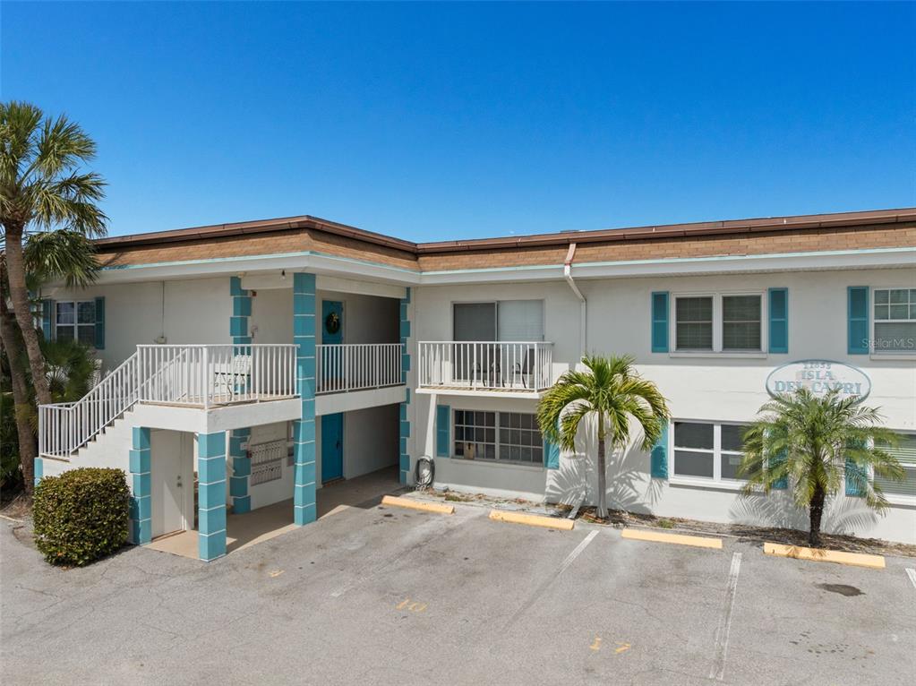A two-story apartment building with white stucco walls, teal accents, and a parking lot — 11655 3RD STREET E UNIT 1, TREASURE ISLAND, FL