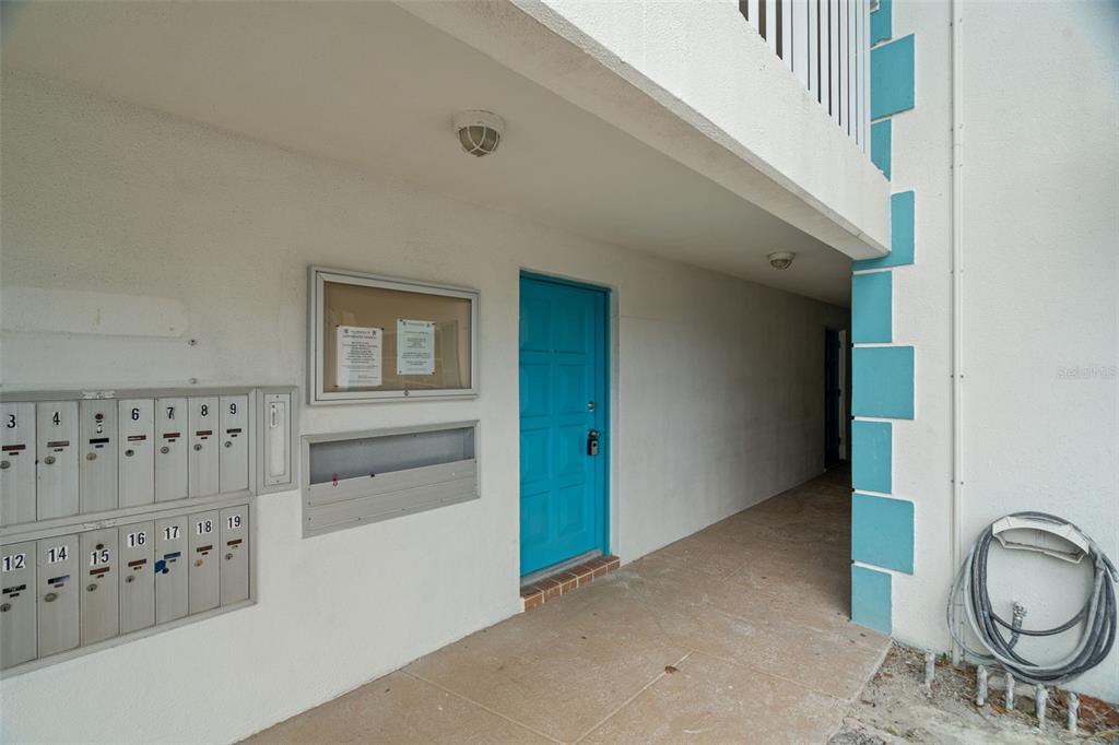 An outdoor hallway features a blue door, a wall-mounted mailbox unit, and a bulletin board — 11655 3RD STREET E UNIT 1, TREASURE ISLAND, FL