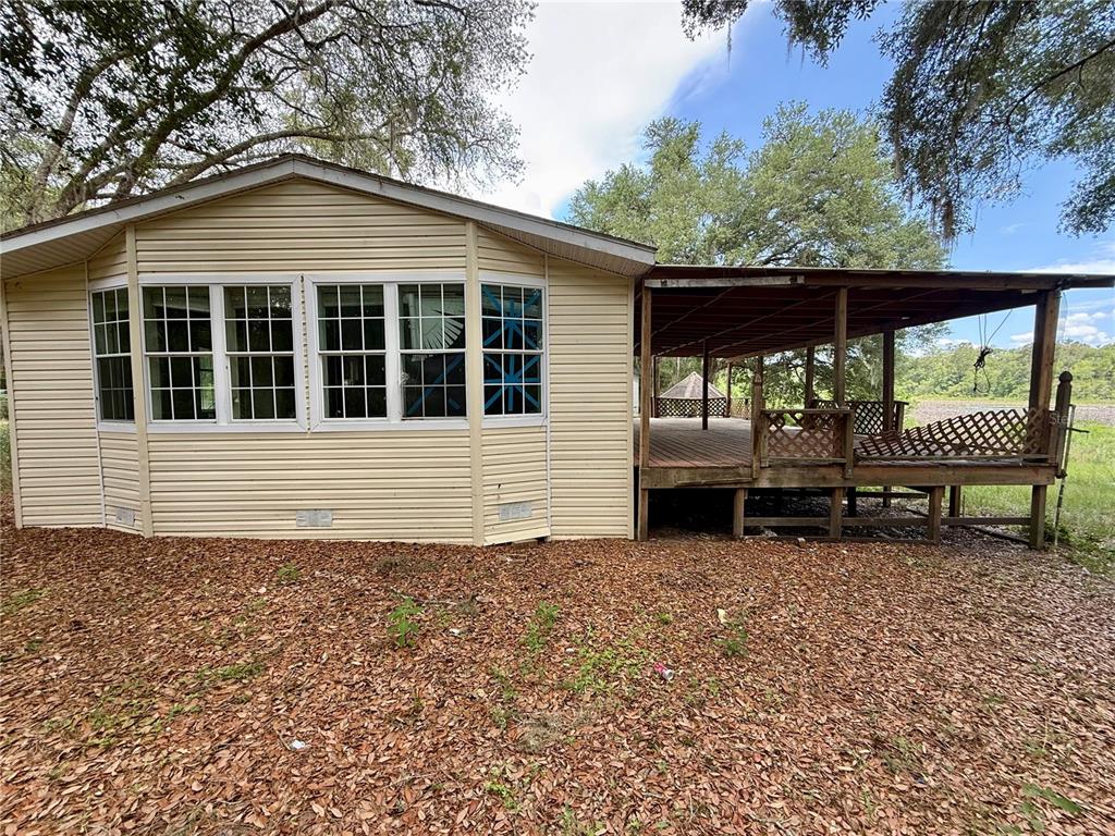 A beige vinyl-sided house features a large attached wooden deck overlooking a grassy area — 5756 NE 165TH TERRACE ROAD, SILVER SPRINGS, FL