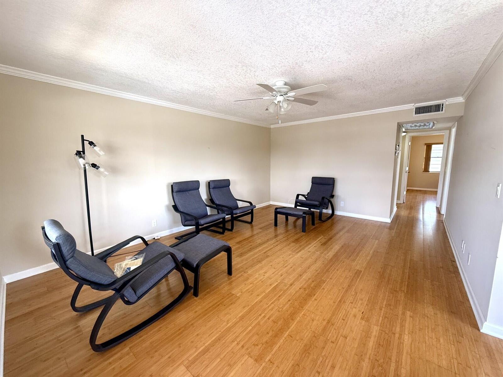 A living room with light walls, bamboo flooring, a ceiling fan, and four dark chairs — 73 Hastings E, West Palm Beach FL 33417, WEST PALM BEACH, FL